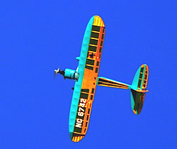 The Phoenix Rainbow trainer plane in orange and turquoise banking towards the camera against a deep blue sky