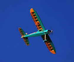 The Phoenix Rainbow trainer plane in orange and turquoise banking away from the camera against a deep blue sky